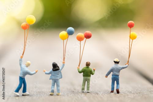 Family and kid concept. Group of children miniature figure with colorful balloons standing, walking and playing together on wooden table.