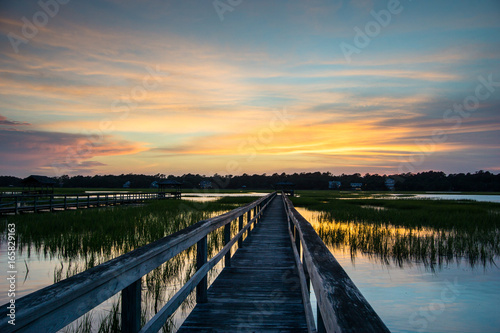 boardwalk leading into tidal basin of a barrier island filled with marsh grass under a beautiful sky at sunset in South Carolina