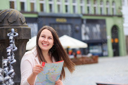 Pretty young brunette female tourist with a map discovering history foreign city, looking to monuments