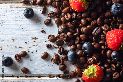 Roasted coffee beans with blueberries and strawberries over a white wood table