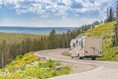 Camper Driving Down Road in The Beautiful Countryside Among Pine Trees and Flowers.