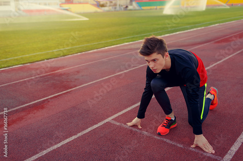 Young athlete runner in a position of readiness to start running in a sports stadium