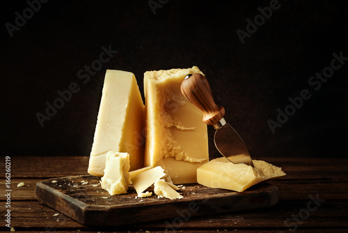 Parmesan cheese on wooden board. Pieces of cheese parmesan on wooden table and cheese knife. Vintage view.