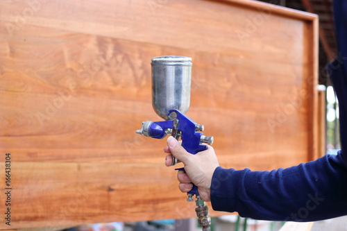 Hands of industrial worker applying spray paint gun with a wooden furniture the workshop background.