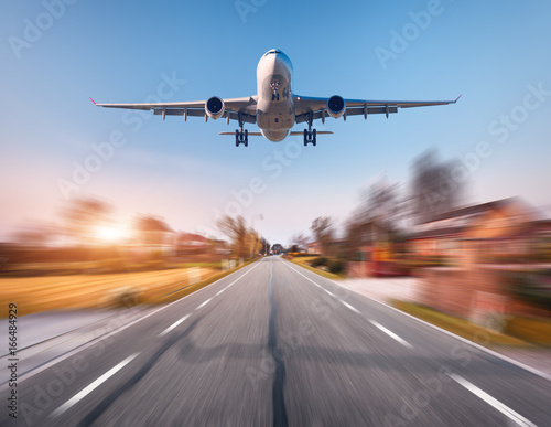 Passenger airplane with motion blur effect. Airplane is flying in the sunset sky over the rural asphalt road at sunset in Netherlands. Landing airplane with blurred background. Aircraft. Business trip