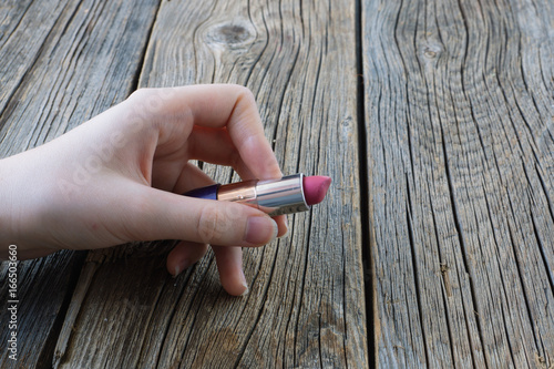Lipstick in hand on wooden background