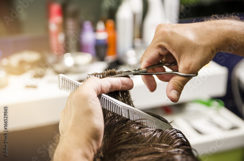 Closeup of hair dresser hands cutting hair with comb and scissors, hair products blurred in background 