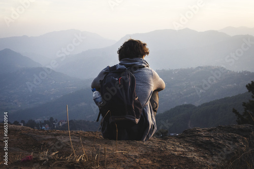 Chico joven de espaldas contemplando las montañas en soledad