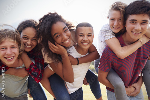 Teenage school friends having fun piggybacking outdoors