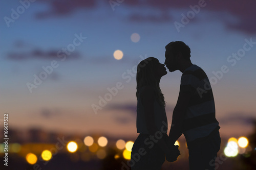 Silhouettes of a young couple kissing with city panorama in the background.