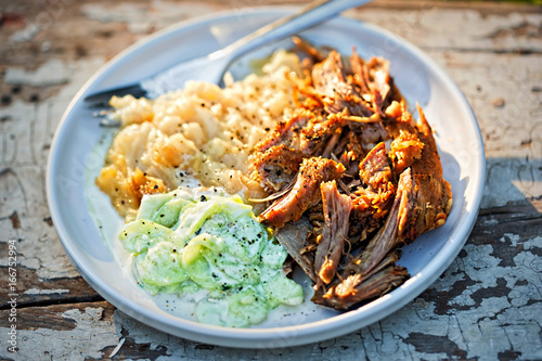 Pulled, seasoned pork, with mashed fried potatoes and cucumber and sour cream salad 