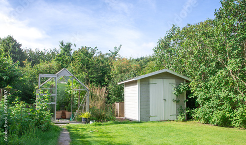 Greenhouse and shed in green lush garden