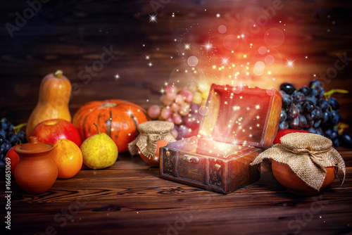 thanksgiving concept of pumpkins, apple, garlic, straw and opened chest treasure with mystical miracle light on wooden table, beautiful fine art design