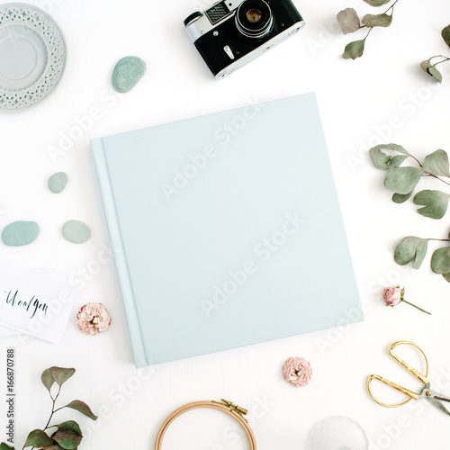 Blue family or wedding photo album with blank space for text, eucalyptus leaf, retro camera and dry rose buds on white background. Flat lay, top view.