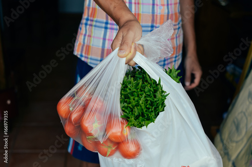 Closeup on man hand holding shopping bag with vegetables green grocery. Consumerism, merchandise variety background