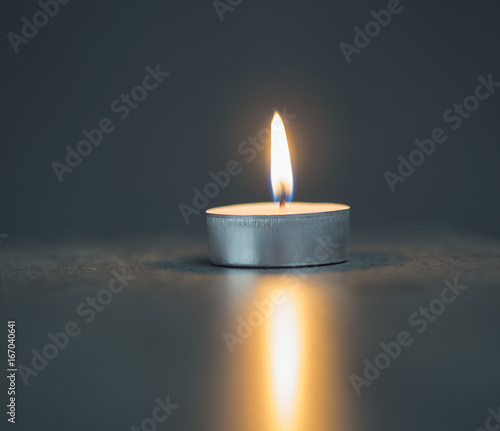 single tea light candle on the soft blurred grey background