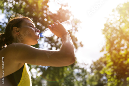 Young beautiful brunette drinking water from a bottle after running workout