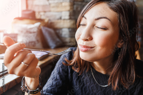 beautiful young asian woman sitting in a cafe and eating delicious cake