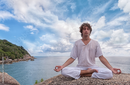 Young man meditating on a high cliff above the sea in the Lotus position