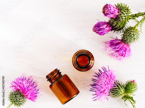 burdock oil in small glass bottle and burdock flowers on white wooden table. Top view or flat lay. Copy space.