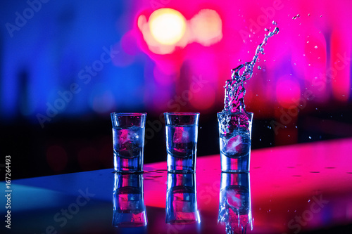  A glass of vodka with ice on the bar, on a red background