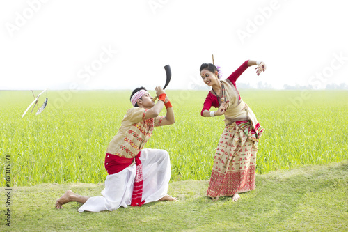 Bihu man blowing on a pepa while Bihu woman dances to his tune 
