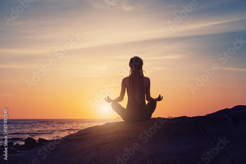 silhouette of Young woman sitting back, meditate in lotus yoga pose outdoor, on the beach