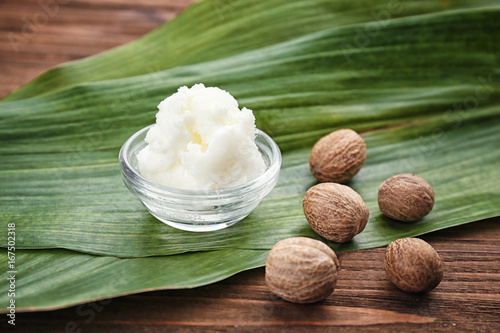 Shea butter in bowl and nuts on wooden table