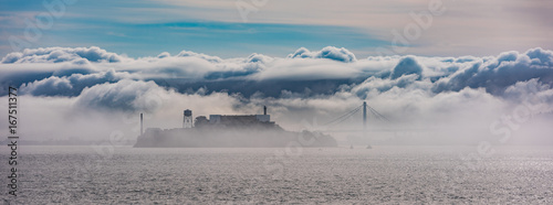 Alcatraz and the Oakland Bay Bridge through the clouds and fog.