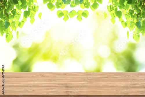 Brown wood table and green leaves hanging with nature bokeh in background. Empty table for display product.