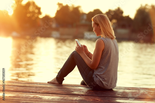Girl with cellphone sitting on dock