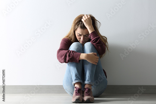 Front view of a sad woman sitting on the floor