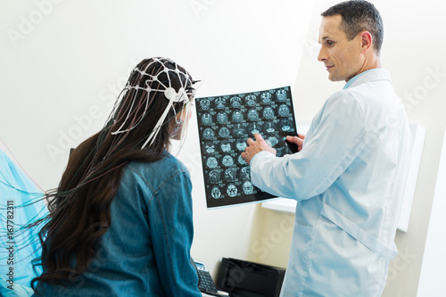 Doctor showing CT scan results to patient undergoing electroencephalography