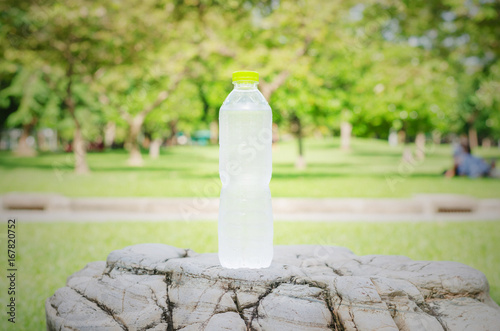 drinking water in plastic bottle on the rock in the park with green background.