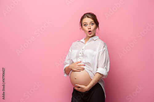 Young beautiful pregnant woman standing on pink background