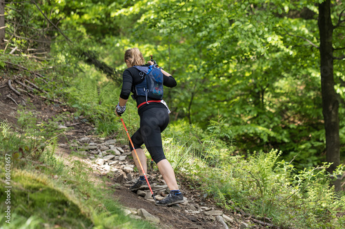 nice young woman with hiking poles walking up the hill in spring green forest