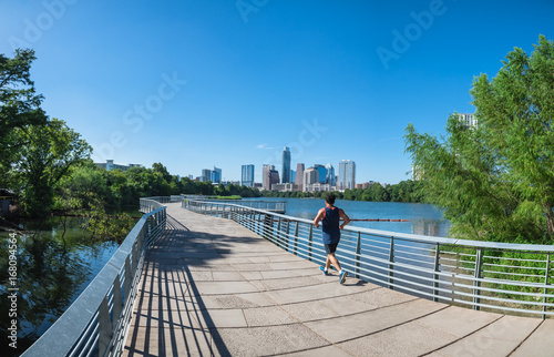 Panorama view Downtown Austin, Texas, US along Colorado River at daytime with cloud blue sky. View from Ann and Roy Butler Hike-and-Bike Trail and boardwalk at Lady Bird Lake, unidentified man running