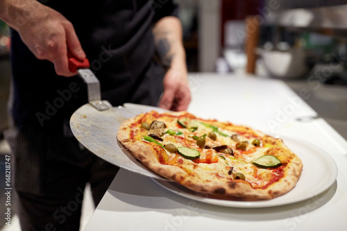 cook with baked pizza on peel at pizzeria