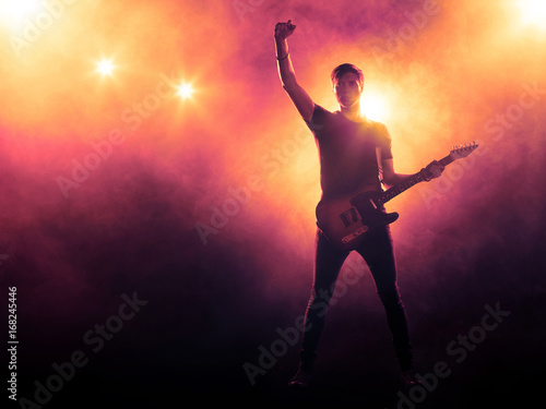 Silhouette of guitarist on stage on smoky background with spotlights 