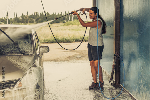 Young man cleaning his car using high pressure water in self-service car wash