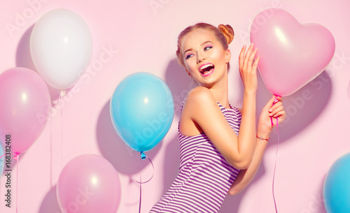 Beauty joyful teenage girl with colorful air balloons having fun over pink background