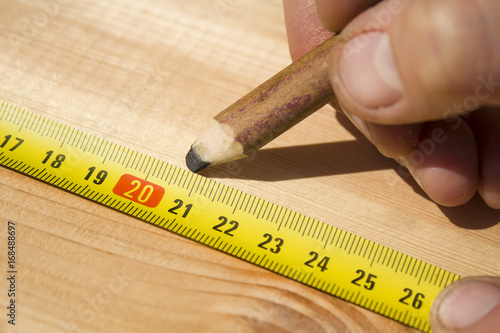Stolarz odmierza odległość za pomocą miary i zaznacza za pomocą ołówka stolarskiego.