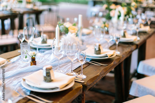 celebration, supper, restaurant business concept. oaken table covered with white tableware lying in center and served for starting banquet and decorated with beautiful small bunches and transparent