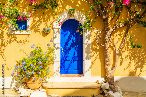 Blue door of a yellow Greek house decorated with flowers, Assos town, Kefalonia island, Greece