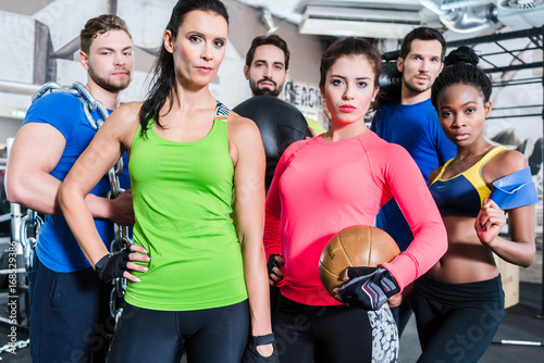 Gruppe Frauen und Männer im Fitnessstudio beim Sport stehen beieinander mit Geräten und Hanteln