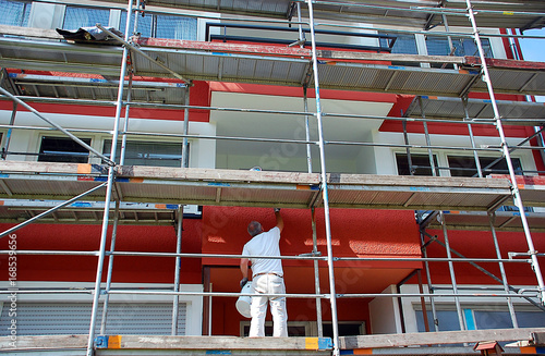 Maler auf Gerüst streicht die Außenfassade eines Mehrfamilienhauses