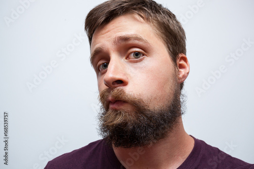Young bearded man looking at his messy long beard and moustache in the mirror