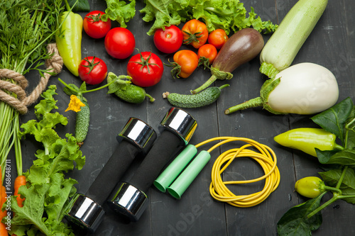 Fresh vegetables and dumbbells. Diet, healthy lifestyle on a black background