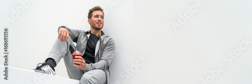 Healthy sport man drinking red smoothie breakfast juice banner panoramic crop relaxing sitting at home in casual activewear sitting on outdoor gym health club, white background.