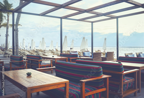 Cafe and restaurant chairs with table and umbrella at beach. Famous travel destination in Sanur, Bali, Indonesia.